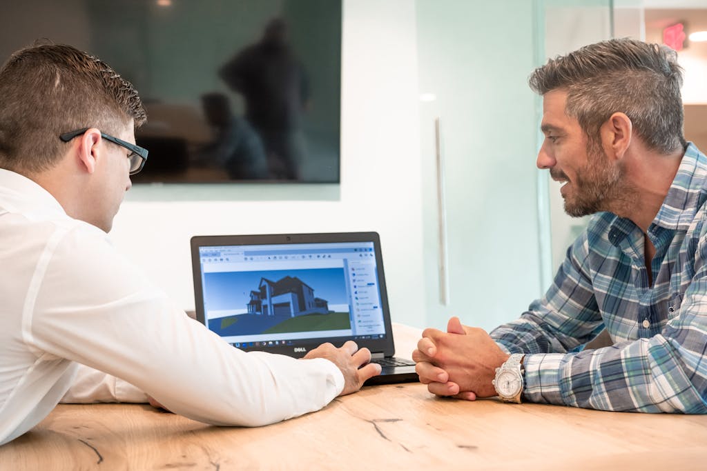 Men Sitting at a Table and Looking at a Laptop Displaying a 3D Project of a House